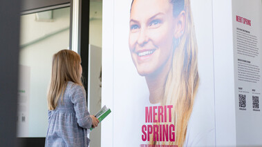 Frau betrachtet das Porträt von Merit Springer auf einer Ausstellungswand mit Beschreibungstext.